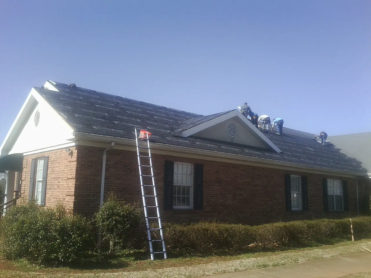 Crew tearing shingles off a brick ranch roof with a ladder set — Emergency Roof Repair work by our crew in La Porte