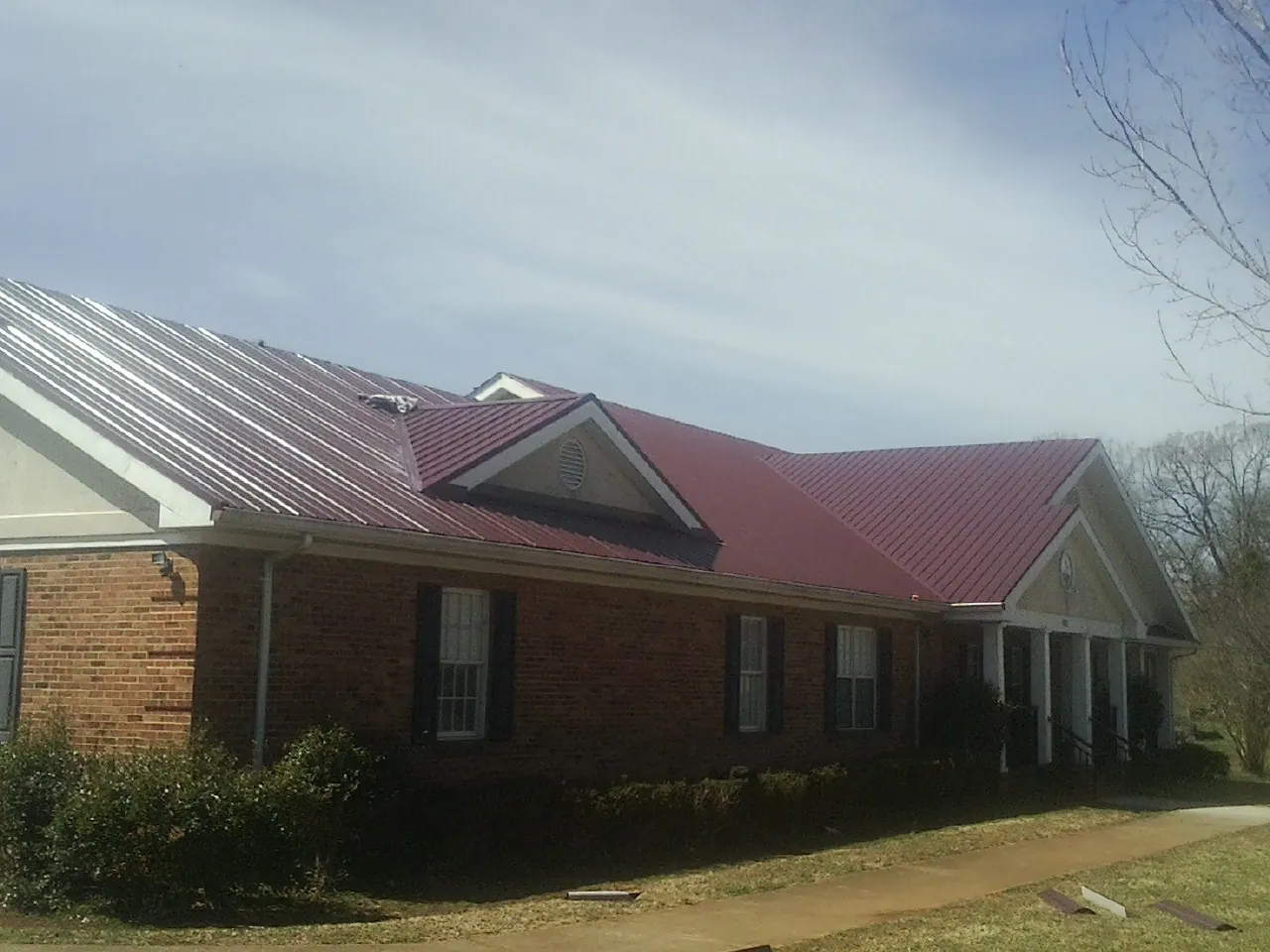 Red metal roof with gabled entries on a long brick building, from a Hail Damage Roof Repair job in La Porte